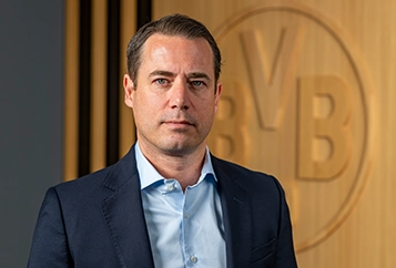 Lars Ricken – Managing Director – in a dark suit with a dark tie looks straight at the camera (photo)